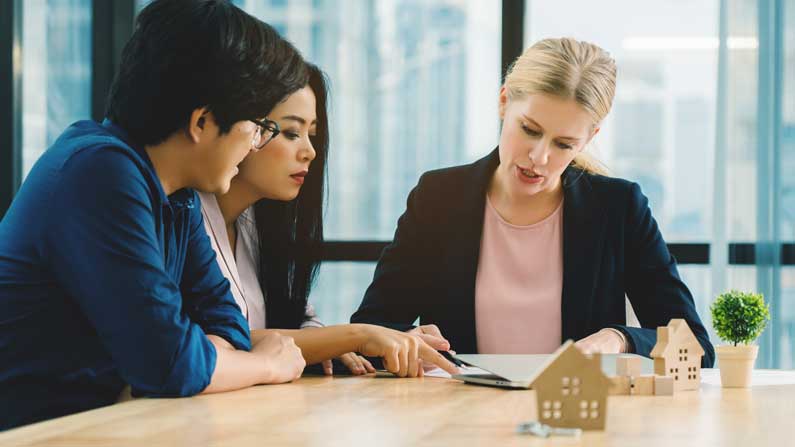 Three people discussing installement loans in Utah at a table, with a model house as a visual aid.