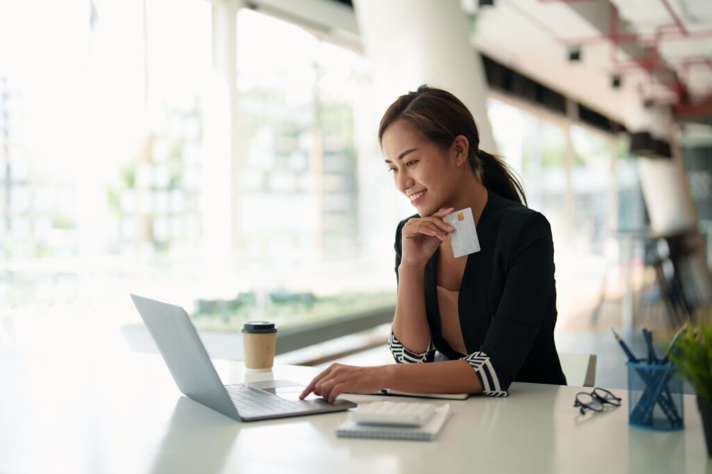 Asian businesswoman making online payday loan payment with credit card on laptop