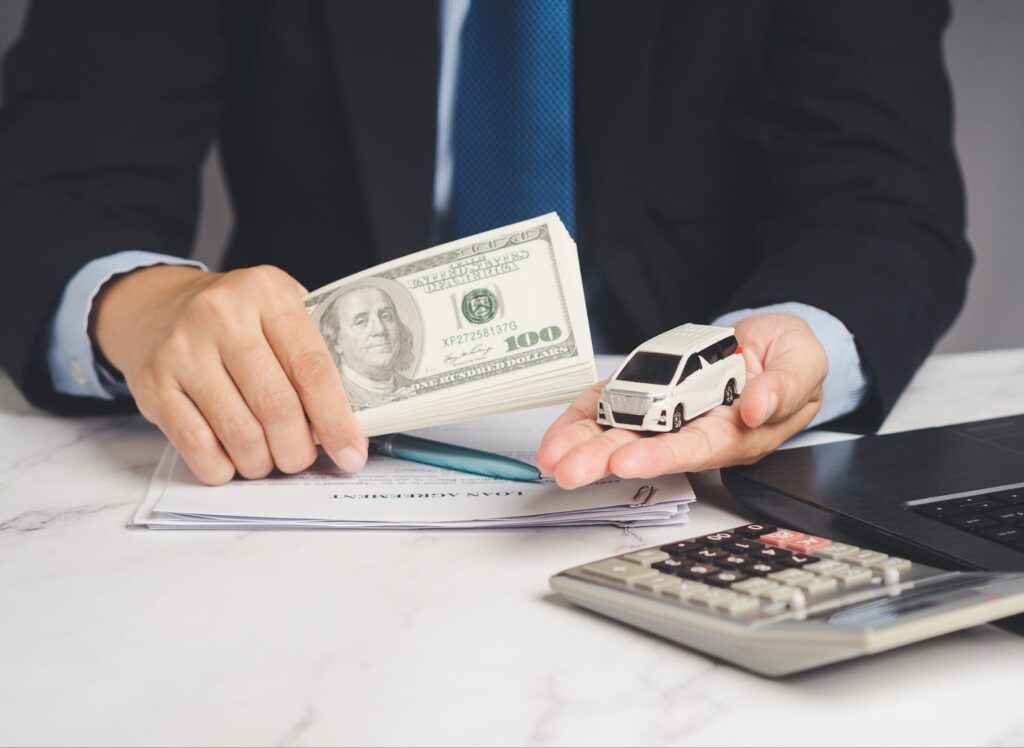 A businessman holding money and car in front of laptop, representing title loans and car title loans.