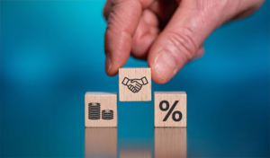 Hand holding wooden blocks with percent sign and coins on blue background. Symbolizing financial growth and savings.