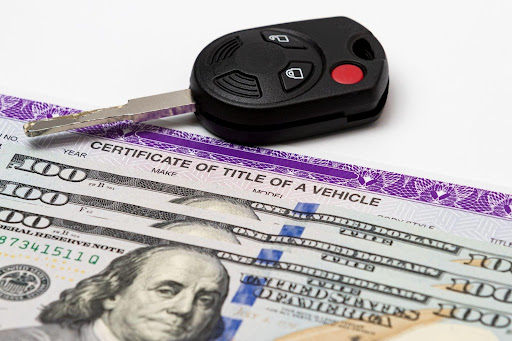 A car key and a key fob resting on a stack of cash, symbolizing wealth and vehicle ownership