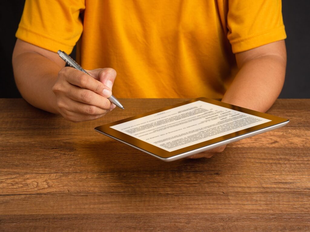 A man engaged in writing on a tablet PC with a pen, set on a wooden table, symbolizing digital financial solutions.