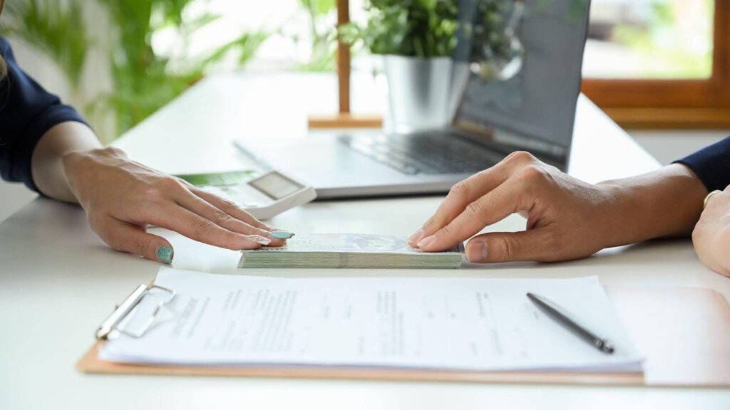 Two people are engaged in a cash exchange at a desk, indicating a transaction