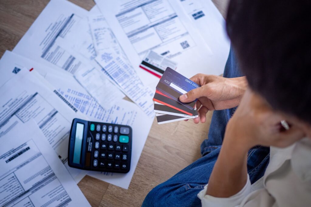 A man on the floor with a credit card and calculator, surrounded by piles of papers, reflecting financial emergencies and payday loans.