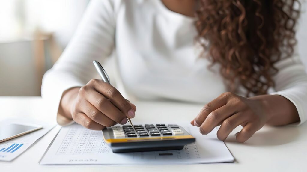 A woman in a white long-sleeve shirt using a calculator while analyzing financial documents on a desk.