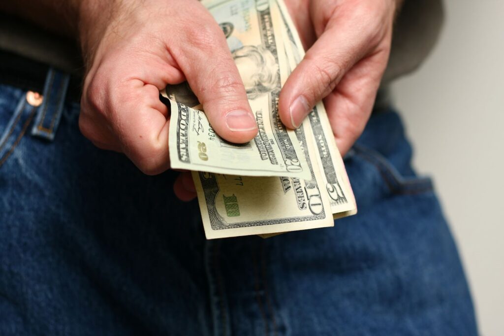 A person holds several U.S. dollar bills while wearing blue jeans.