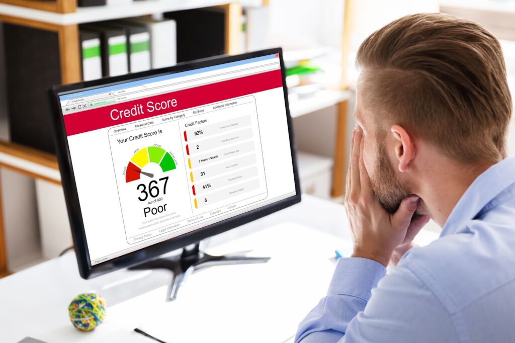 Man looking at a computer screen displaying a credit score of 367 rated as "Poor" in an office setting.