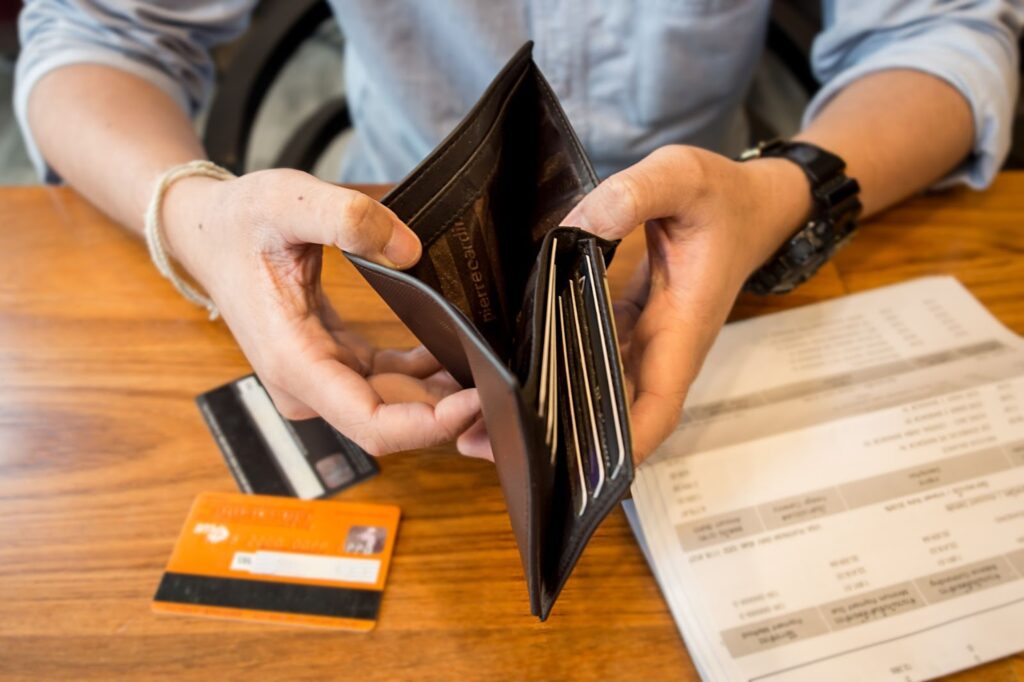 Person holding an open empty wallet with credit cards and a bill on a wooden table.