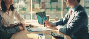 Three business professionals seated at a table collaborating over a laptop during a meeting