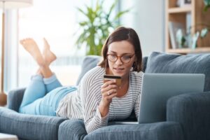 Woman lying on a sofa using a laptop and holding a credit card