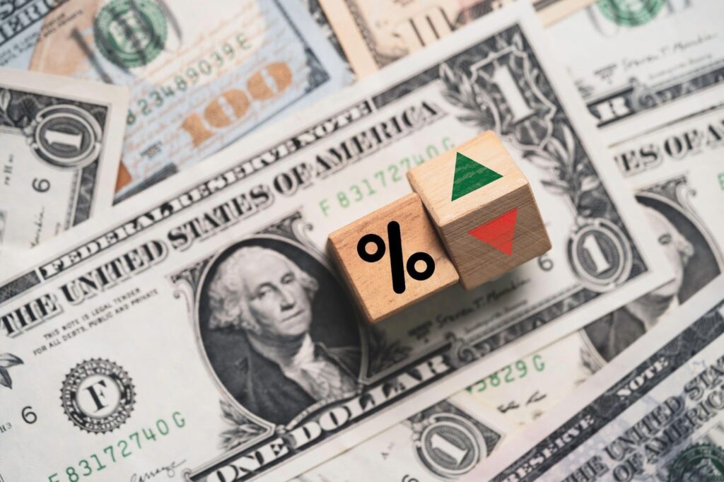 Wooden blocks with a percent sign and arrows rest on U.S dollar bills