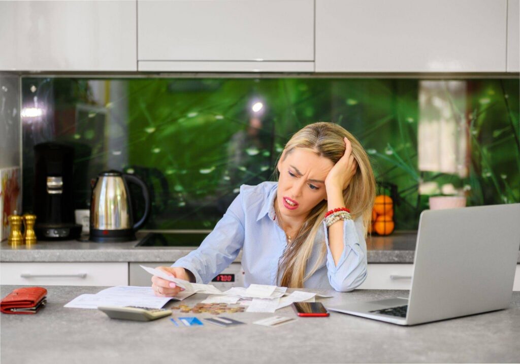 A woman sits at a kitchen counter looking frustrated while examining bills