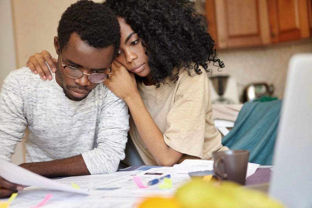 A stressed young couple reviewing financial documents and bills together at home.