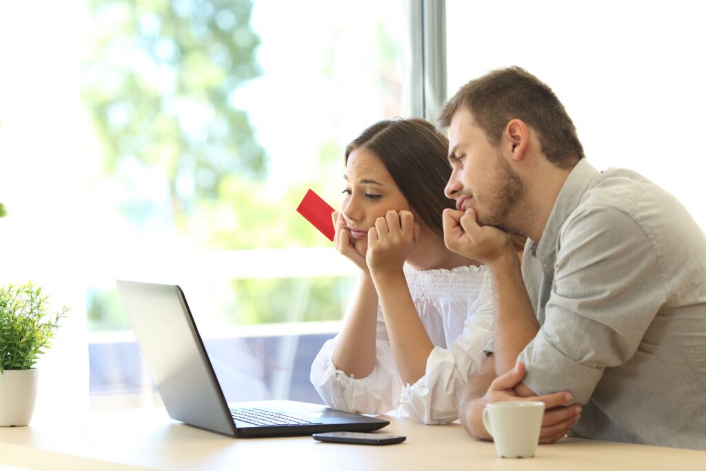 A worried couple holding a credit card while looking at a laptop screen.