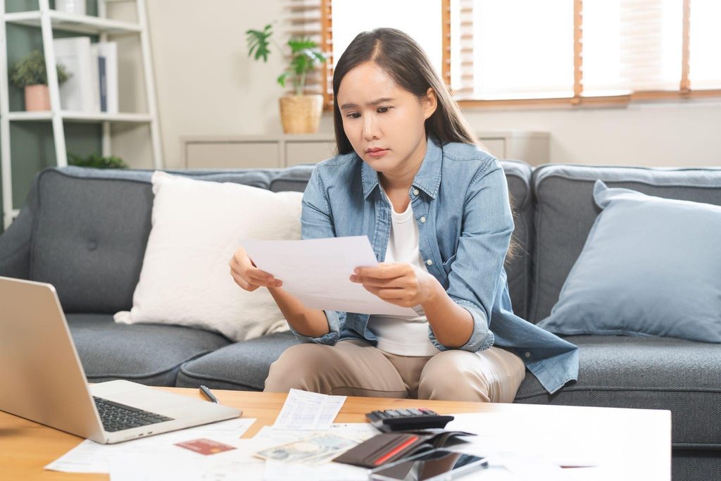 Woman sitting on a couch working on a laptop with papers spread out beside her