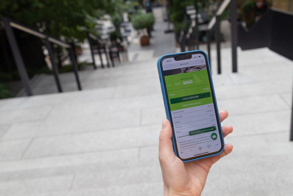 A hand holds a smartphone showing a green and white app on its screen